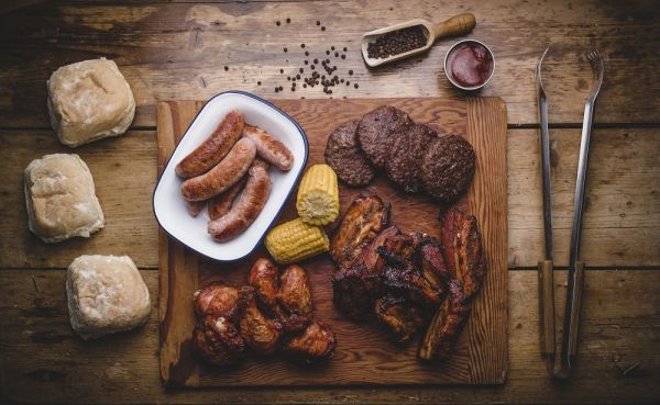A wooden board of Aune Valley sausages, burgers, smoked ribs and baps, photographed overhead